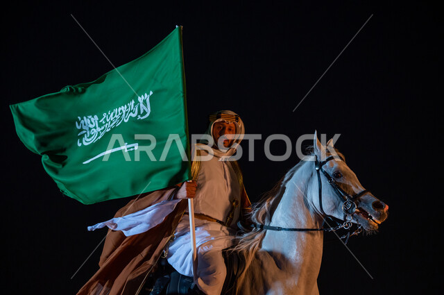 Practicing the hobby of raising horses, the anniversary of the founding of the Kingdom, February 22, Flag Day, March 11, celebration of the Saudi National Day, September 23, a picture from the side of a Saudi Gulf Arab man wearing the uniform of the Founding Day 1727 AD, riding an Arabian horse and holding the flag of the Kingdom in his hand, the passion for raising purebred horses.