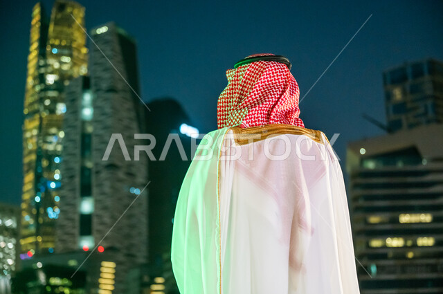 ارتداء زي المناسبات التقليدية، الاستمتاع بالخروج في الهواء الطلق, الوقوف لتأمل التطور العمراني في مدينة الرياض, صورة من الخلف لرجل عربي خليجي سعودي يرتدي الشماغ والبشت, مركز الملك عبد الله المالي (كافد). 