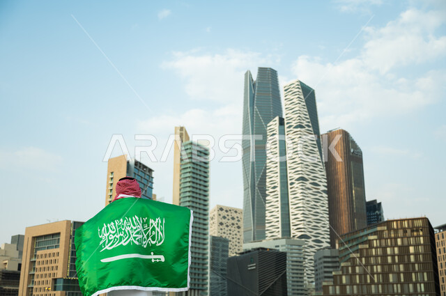 رفع العلم على الأكتاف احتفالا بالعيد الوطني, تمجيد اليوم الوطني في 23 سبتمبر, يوم العلم السعودي 11 مارس, رجل عربي سعودي خليجي يرتدي الزي التقليدي يشارك بالمناسبات والأعياد الوطنية, خلفية أبراج الملك عبدالله