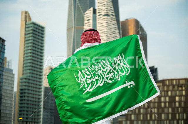 تمجيد اليوم الوطني في 23 سبتمبر , رفع العلم على الأكتاف احتفالا بالعيد الوطني , يوم العلم السعودي 11 مارس, صورة مقربة لرجل عربي سعودي خليجي يرتدي الزي التقليدي يشارك بالمناسبات والأعياد الوطنية, خلفية أبراج الملك عبدالله