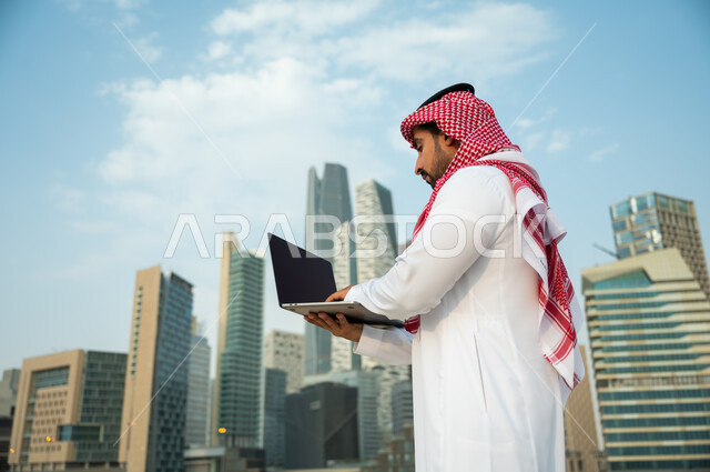 Making successful business deals with businessmen via the Internet, working remotely through social media, a close-up of a Saudi Arabian Gulf man wearing a thobe and a head scarf using a computer, modern electronic applications and job opportunities on th