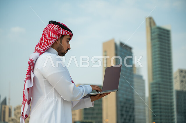 صفقات عمل ناجحة مع رجال أعمال عبر الأونلاين, العمل عن بعد عبر مواقع التواصل الاجتماعي, صورة مقربة لرجل عربي سعودي خليجي يرتدي الثوب والشماغ يقوم باستخدام جهاز الحاسوب, التطبيقات الالكترونية الحديثة وفرص العمل على الانترنت, أبراج الملك عبدالله المالية