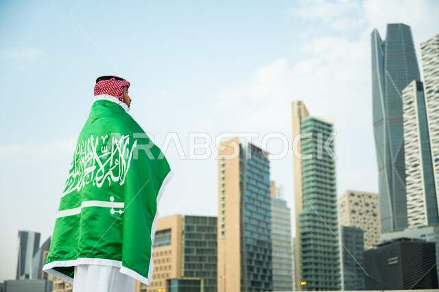 التعبير عن الحب والولاء في يوم العلم 11 مارس, الوقوف بافتخار بذكرى اليوم الوطني 23 سبتمبر , ارتداء العلم السعودي بتقدير واحترام, رجل عربي سعودي خليجي يرتدي الثوب والشماغ التقليدي يشارك في الأعياد والمناسبات الوطنية السعودية
