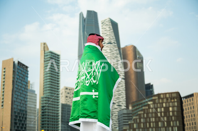 الوقوف بافتخار بذكرى اليوم الوطني 23 سبتمبر , ارتداء العلم السعودي بتقدير واحترام, التعبير عن الحب والولاء في يوم العلم 11 مارس, رجل عربي سعودي خليجي يرتدي الثوب والشماغ التقليدي يشارك في الأعياد والمناسبات الوطنية السعودية