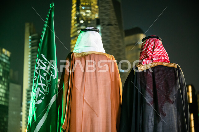 The concept of patriotism, expression of belonging and loyalty on Flag Day, March 11, celebration of the National Day, September 23, costumes for popular occasions and celebrations, a picture from the back of two Saudi Arab men and two Gulf men wearing traditional Saudi clothing, financial and economic horoscopes at night.