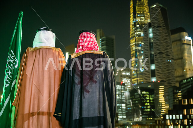 The concept of patriotism, expression of belonging and loyalty on Flag Day, March 11, celebration of the National Day, September 23, costumes for popular occasions and celebrations, a picture from the back of two Saudi Arab men and two Gulf men wearing traditional Saudi clothing, financial and economic horoscopes at night.