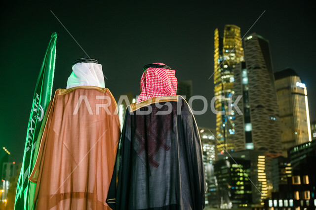 The concept of patriotism, expression of belonging and loyalty on Flag Day, March 11, celebration of the National Day, September 23, costumes for popular occasions and celebrations, a picture from the back of two Saudi Arab men and two Gulf men wearing traditional Saudi clothing, financial and economic horoscopes at night.
