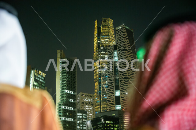 المركز الاقتصادي المالي (كافد) في المملكة العربية السعودية، ارتداء زي المناسبات التقليدية، الاستمتاع بالخروج في الهواء الطلق, صورة مقربة من الخلف لرجلين عربيين خليجيين سعوديين يقفان ويتأملان التطور العمراني في مدينة الرياض
