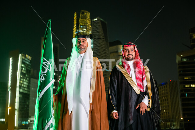 الاحتفال بذكرى اليوم الوطني 23 سبتمبر , أزياء المناسبات والاحتفالات الشعبية, التعبير عن الحب والولاء في يوم العلم 11 مارس, رجلان عربيان سعوديان خليجيان يرتديان الزي السعودي التقليدي، الوقوف باعتزاز بالدولة السعودية، خلفية المركز المالي (كافد)في الرياض
