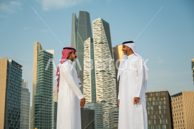 محادثات ودردشات في وضح النهار, إيماءات تدل على السرور برؤية الأصدقاء, التعارف وبناء علاقات اجتماعية, إجراء محادثات عمل ناجحة في الخارج, رجلان عربيان سعوديان خليجيان يرتديان الزي التقليدي يقومان بمقابلة بعضهما, خلفية مركز الملك عبد الله المالي (كافد)