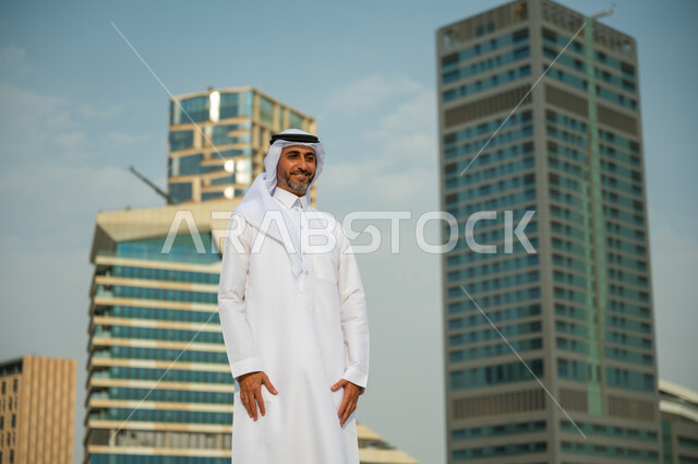 معالم وأماكن سياحية في الرياض, إيماءات الافتخار و الاعتزاز بتطور المملكة, الأبراج المالية الاقتصادية في الرياض، رجل عربي خليجي سعودي مبتسم يرتدي الغترة والعقال يقف باستقامة وينظر الى الكاميرا، االنمو العمراني السعودية، خلفية مركز الملك عبد الله المالي