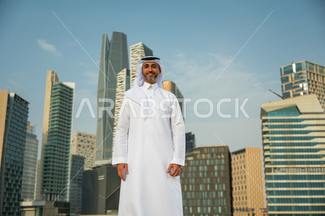 معالم وأماكن سياحية في الرياض, إيماءات الافتخار و الاعتزاز بتطور المملكة, الأبراج المالية الاقتصادية في الرياض، رجل عربي خليجي سعودي مبتسم يرتدي الغترة والعقال يقف باستقامة وينظر الى الكاميرا، االنمو العمراني السعودية، خلفية مركز الملك عبد الله المالي