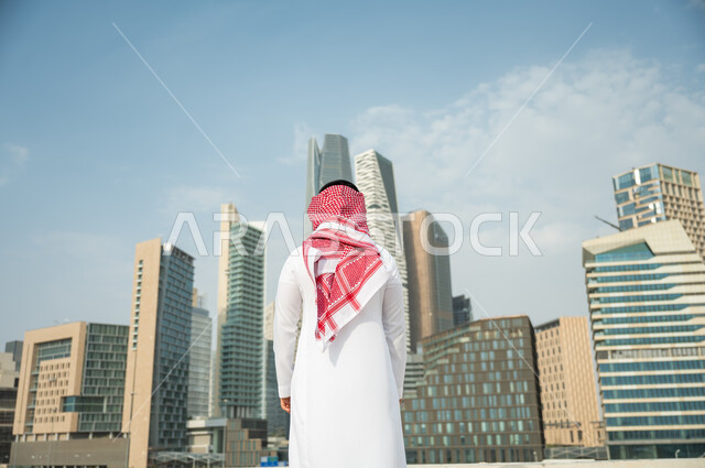 التطور و الفن الهندسي المعماري المتميز في الرياض, الوقوف أمام ناطحات السحاب  في الرياض، صورة من الخلف لرجل عربي خليجي سعودي يرتدي الشماغ والثوب التقليدي و يقف باستقامة وشموخ، التطور العمراني السعودي، خلفية مركز الملك عبد الله المالي