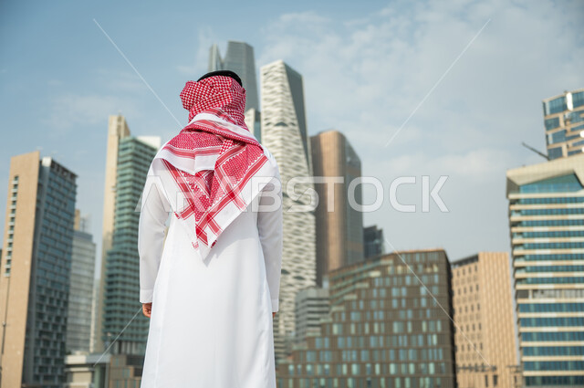 التطور و الفن الهندسي المعماري المتميز في الرياض, الوقوف أمام ناطحات السحاب  في الرياض، صورة من الخلف لرجل عربي خليجي سعودي يرتدي الشماغ والثوب التقليدي و يقف باستقامة وشموخ، التطور العمراني السعودي، خلفية مركز الملك عبد الله المالي