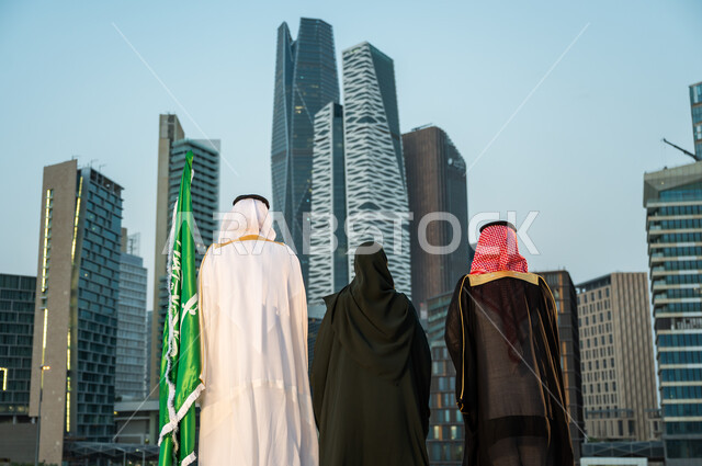 تأمل الأبراج والمنشآت في مدينة الرياض وضح النهار, الاحتفال بالمناسبات الوطنية السعودية, ارتداء الأزياء الشعبية التقليدية, صورة من الخلف لمواطنين عرب سعوديين خليجيين يحتفلون باليوم الوطني 23 سبتمبر, الوقوف بثقة في يوم العلم 11 مارس