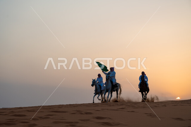 أنشطة وفعاليات ركوب الجياد في الصحراء، ذكرى اليوم الوطني السعودي 8 ربيع الأول، رفع الراية للاحتفال بيوم العلم السعودي 11 مارس، مجموعة رجال عرب خليجيون سعوديون يتجولون على ظهر الاحصنة وقت غروب الشمس، حب وعشق الخيل السعودي الأصيل.