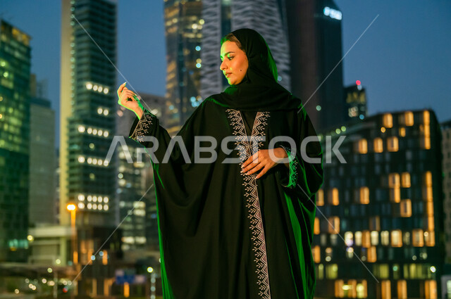 النظر إلى تطريز العباءة والإعجاب بها, انعكاس الضوء الأخضر على مواطنة عربية خليجية سعودية تشارك في المناسبات الوطنية, ارتداء الأزياء السعودية التقليدية في ذكرى اليوم الوطني 23 سبتمبر, يوم العلم السعودي 11 مارس, الأبراج والمباني المضاءة في مدينة الرياض