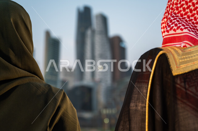 Wearing traditional folk costumes, enjoying the outdoors, standing in front of skyscrapers in Riyadh, a close-up image of a Saudi Arabian Gulf man and woman having fun, background of towers and economic buildings, famous places and tourist attractions in