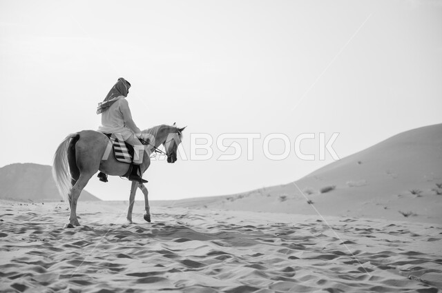 ممارسة هواية ركوب الأحصنة، صورة بالأبيض والأسود لفارس عربي خليجي سعودي يركب الفرس العربي الأصيل، توارث شغف الجياد من الأجداد، حب وعشق الخيل السعودي الأصيل، أنشطة وفعاليات ركوب الجياد، التجول على ظهر الحصان، الكثبان الرملية الناعمة في صحراء السعودية