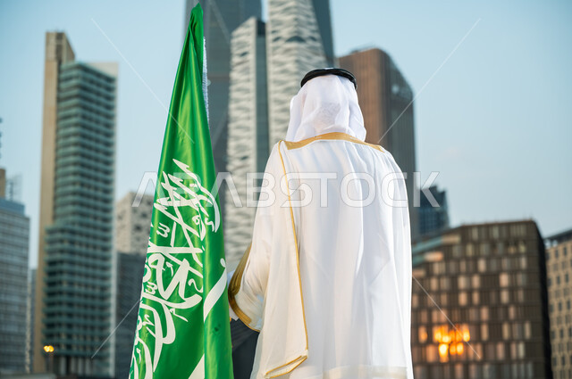 الاعتزاز بالتطور العمراني للمنشآت الاقتصادية, يوم العلم 11 مارس, الاهتمام بالمركز المالي في الرياض, الاحتفال باليوم الوطني 23سبتمبر أمام أبراج كافد, صورة مقربة من الخلف لرجل عربي سعودي خليجي يرتدي البشت والغترة التقليدية ينظر إلى الأبراج المالية