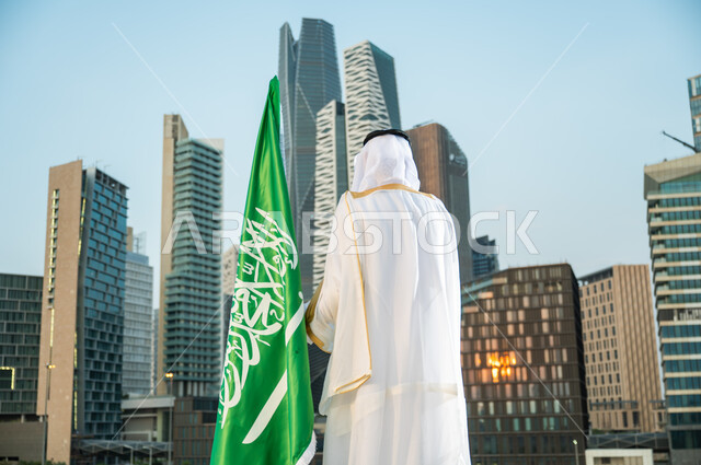 الاهتمام بالمركز المالي في الرياض, الاحتفال باليوم الوطني 23 سبتمبر أمام أبراج كافد, صورة من الخلف لرجل عربي سعودي خليجي يرتدي البشت والغترة التقليدية السعودية ينظر إلى الأبراج المالية, يوم العلم 11 مارس, الفخر بالتطور العمراني للمنشآت الاقتصادية