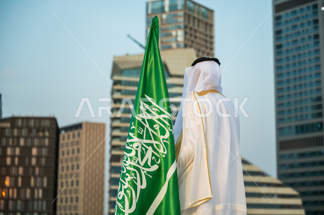 يوم العلم 11 مارس, الاهتمام بالمركز المالي في الرياض, الاحتفال باليوم الوطني23 سبتمبر أمام أبراج كافد, صورة مقربة من الخلف لرجل عربي سعودي خليجي يرتدي البشت والغترة التقليدية السعودية ينظر إلى الأبراج المالية, الفخر بالتطور العمراني للمنشآت الاقتصادية
