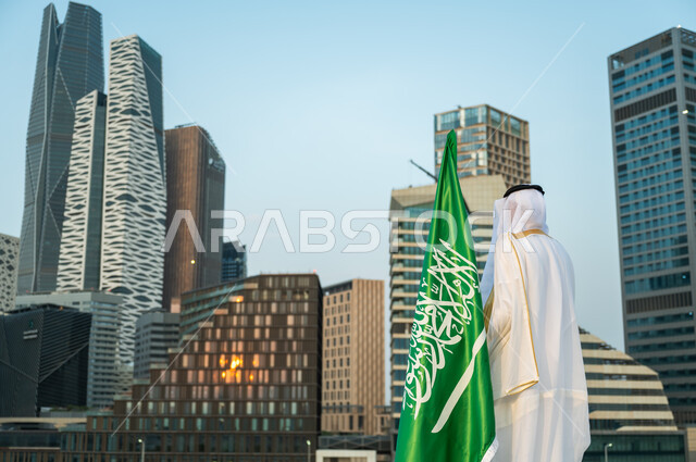 الاهتمام بالمركز المالي في الرياض, الاحتفال باليوم الوطني 23 سبتمبر أمام أبراج كافد, صورة من الخلف لرجل عربي سعودي خليجي يرتدي البشت والغترة التقليدية السعودية ينظر إلى الأبراج المالية, يوم العلم 11 مارس, الفخر بالتطور العمراني للمنشآت الاقتصادية