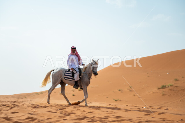 Passion for equestrian and practicing the hobby of riding horses, a Saudi Arabian Gulf man wanders in the Saudi desert on the back of an authentic Arabian horse, the love of horses was inherited from the ancestors and spread among the people of the countr