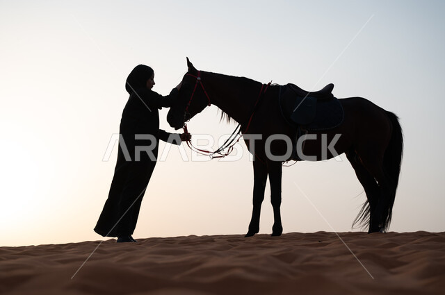 شغف الفروسية وهواية ركوب الأحصنة، نشر حب الخيل بين أبناء الوطن السعودي، اهتمام وحب النساء بتربية ورعاية الجياد في المملكة العربية السعودية، صورة ظلية بالأبيض والأسود لشابة عربية سعودية خليجية محجبة تقوم بمداعبة جوادها العربي الأصيل، سيلوييت.