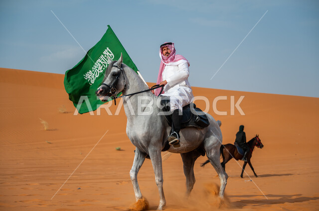شغف الفروسية وممارسة هواية ركوب الخيل في الصحراء، فارس عربي خليجي سعودي يمتطي الفرس العربي الأصيل ويرفع علم السعودية، العيد الوطني السعودي، اليوم الوطني السعودي 23 سبتمبر، يوم العلم 11 مارس، إظهار مشاعر الاعتزاز بالوطن، نشر حب الخيل بين ابناء الوطن