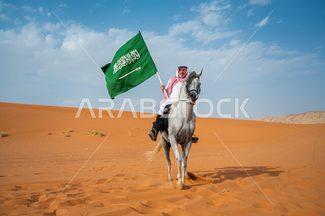 العيد الوطني السعودي، شغف الفروسية وممارسة هواية ركوب الخيل في الصحراء، فارس عربي خليجي سعودي يمتطي الفرس العربي الأصيل ويرفع علم السعودية، اليوم الوطني السعودي 23 سبتمبر، يوم العلم 11 مارس، إظهار مشاعر الاعتزاز بالوطن، نشر حب الخيل بين ابناء الوطن