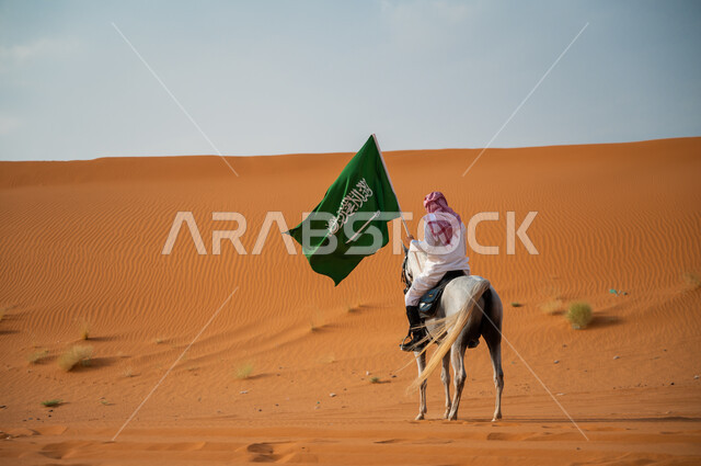 Saudi National Day, the National Day for the Unification of the Kingdom, September 23, a picture from the back of a Saudi Gulf Arab silhouette riding a purebred Arabian horse and raising the Saudi flag, pride in having a Saudi identity, activities and events riding horses in the desert, Flag Day, March 11, inheriting the passion for horses from the ancestors