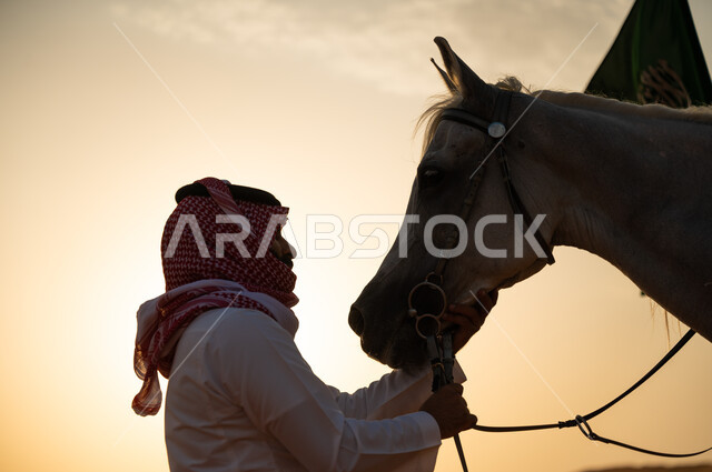 مشاركة الاحتفال باليوم الوطني السعودي مع الخيول العربية، الاعتناء و رعاية الفرس وقت غروب الشمس في الصحراء، فارس عربي خليجي سعودي يرتدي الشماغ والزي التقليدي يمسك بحصان عربي أصيل، ذكرى يوم العلم 11 مارس، العيد الوطني لتوحيد البلاد 8 ربيع الأول