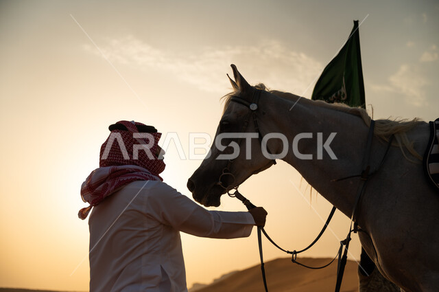 الاعتناء بالفرس وقت غروب الشمس في الصحراء، مشاركة الاحتفال باليوم الوطني السعودي مع الخيول العربية، صورة مقربة لفارس عربي خليجي سعودي يرتدي الشماغ والزي التقليدي يمسك بحصان عربي أصيل، ذكرى يوم العلم 11 مارس، العيد الوطني لتوحيد البلاد 8 ربيع الأول