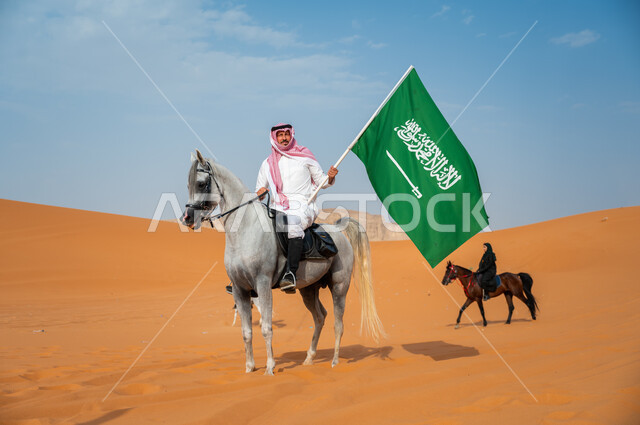 Unification of the Kingdom of Saudi Arabia, a Saudi Gulf Arab man riding a purebred Arabian horse and raising the Saudi flag, commemoration of National Day September 23, Saudi National Day, Flag Day March 11, love and affection for the Saudi horse, passion for equestrianism and practicing the hobby of horse riding