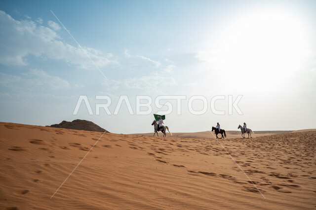 فرسان يمتطون الخيل في الصحراء، إحياء ذكرى اليوم الوطني، مشاركة فعاليات ركوب الخيل في العيد الوطني 8 ربيع الأول، الاحتفال بيوم العلم السعودي 11 مارس، مجموعة رجال عرب خليجيون سعوديون يتسابقون على ظهر الاحصنة ويرفعون علم المملكة، قوة وسرعة الخيل السعودي