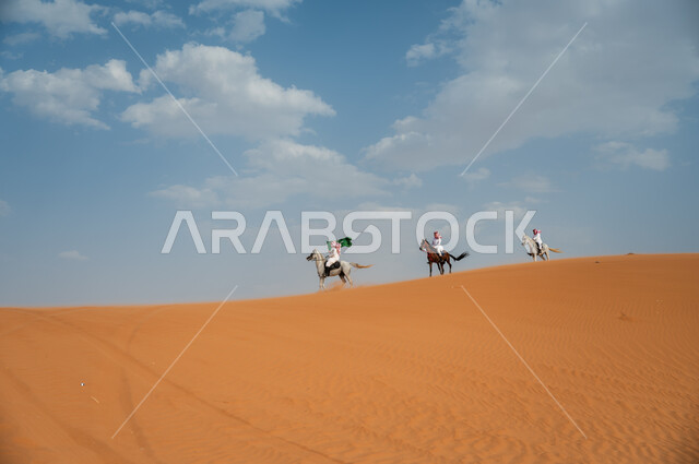 قوة وسرعة الخيل السعودي, مشاركة فعاليات ركوب الخيل في العيد الوطني، هواية امتطاء الجياد في الصحراء، إحياء ذكرى اليوم الوطني 8 ربيع الأول، الاحتفال بيوم العلم السعودي 11 مارس، مجموعة رجال عرب خليجيون سعوديون يتسابقون على ظهر الاحصنة ويرفعون علم المملكة