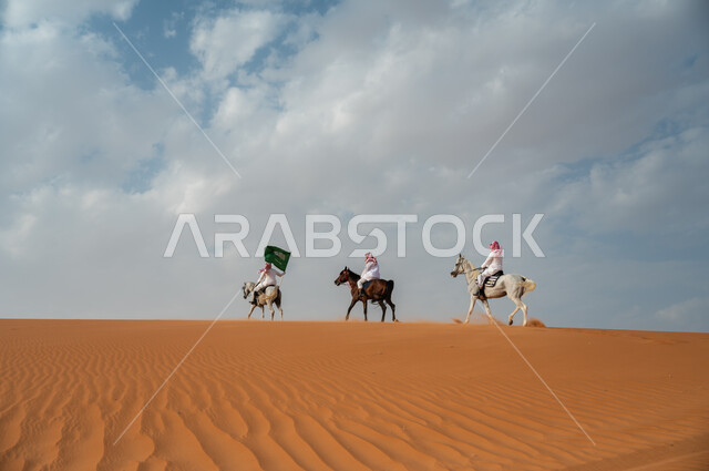 قوة وسرعة الخيل السعودي, مشاركة فعاليات ركوب الخيل في العيد الوطني، هواية امتطاء الجياد في الصحراء، إحياء ذكرى اليوم الوطني 8 ربيع الأول، الاحتفال بيوم العلم السعودي 11 مارس، مجموعة رجال عرب خليجيون سعوديون يتسابقون على ظهر الاحصنة ويرفعون علم المملكة