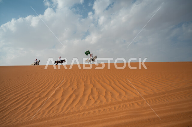 قوة وسرعة الخيل السعودي, مشاركة فعاليات ركوب الخيل في العيد الوطني، هواية امتطاء الجياد في الصحراء، إحياء ذكرى اليوم الوطني 8 ربيع الأول، الاحتفال بيوم العلم السعودي 11 مارس، مجموعة رجال عرب خليجيون سعوديون يتسابقون على ظهر الاحصنة ويرفعون علم المملكة