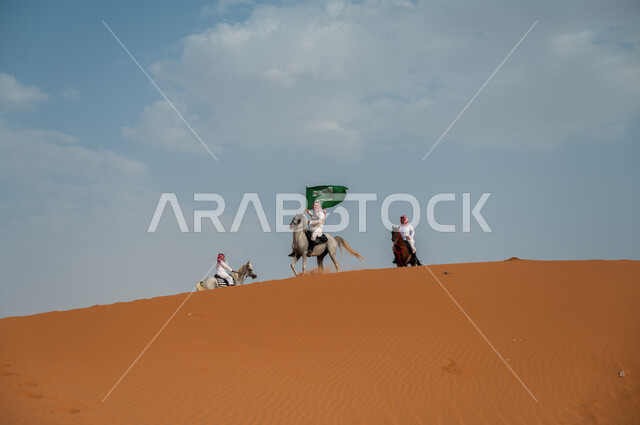 مشاركة فعاليات ركوب الخيل في العيد الوطني، هواية امتطاء الجياد في الصحراء، إحياء ذكرى اليوم الوطني 8 ربيع الأول، الاحتفال بيوم العلم السعودي 11 مارس، مجموعة رجال عرب خليجيون سعوديون يتسابقون على ظهر الاحصنة ويرفعون علم المملكة، قوة وسرعة الخيل السعودي