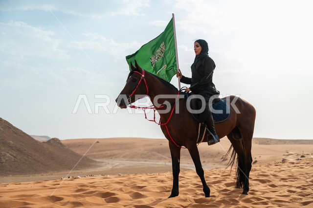 مفهوم الولاء للوطن والمشاركة بالمناسبات و الأعياد الوطنية, سيدة عربية خليجية سعودية محجبة تمتطي الخيل وترفع بيدها علم المملكة في الصحراء, تعميق الانتماء للوطن بالاحتفال بذكرى اليوم الوطني 23 سبتمبر, يوم العلم السعودي 11 مارس