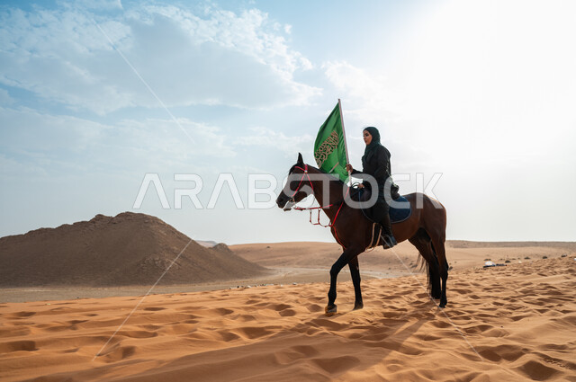 ترسيخ جذور الانتماء الوطني, مشاركة الأحصنة بالمناسبات و الأعياد الوطنية, سيدة عربية خليجية سعودية محجبة تمتطي الخيل وترفع بيدها علم المملكة في الصحراء, الاحتفال بذكرى اليوم الوطني 23 سبتمبر, يوم العلم السعودي 11 مارس, ارتباط الجياد بإرث المملكة