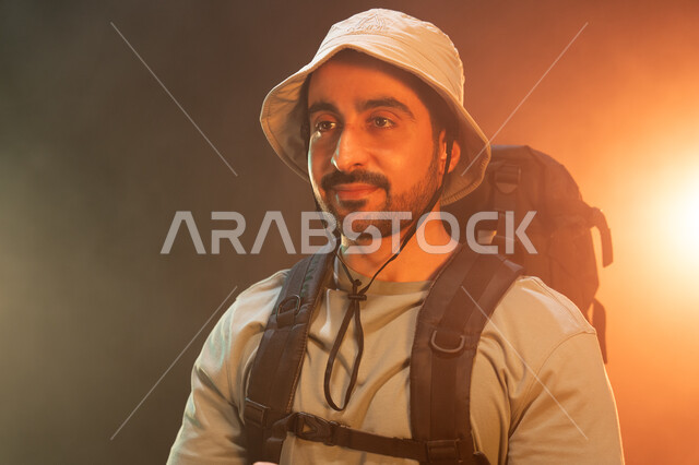 ممارسة هواية رياضة الهايكنغ بإيماءات العزيمة والإصرار, الحفاظ على الصحة واللياقة البدنية, الفعاليات والأنشطة الترفيهيه في السعودية, بورتريه مقرب لشاب عربي سعودي خليجي يرتدي حقيبة معدات التسلق, التدريب على تسلق القمم والمرتفعات, خلفية سوداء مع إضاءة ملونة