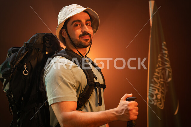 المشاركة بالهوايات الترفيهية الممتعه, يوم العلم السعودي 11 مارس, ممارسة رياضة الهايكنغ للصحة واللياقة البدنية, بورتريه مقرب من الجانب لشاب عربي سعودي خليجي يرتدي زي التسلق يقف أمام علم المملكة, استذكار اليوم الوطني السعودي في 23 سبتمبر