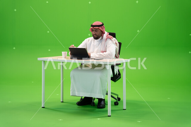 القيام بمحادثات عبر الانترنت, إجراء مقابلات عمل أونلاين, استخدام الأجهزة والتقنيات الحديثة, بورتريه لموظف عربي سعودي خليجي يرتدي الزي التقليدي السعودي يقوم بالعمل داخل مكتبه, مهن ووظائف سعودية, خلفية خضراء, كروما 