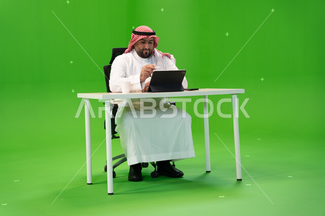 إجراء مقابلات عمل أونلاين, القيام بمحادثات عبر الانترنت, استخدام الأجهزة والتقنيات الحديثة, بورتريه لموظف عربي سعودي خليجي يرتدي الزي التقليدي السعودي يقوم بالعمل داخل مكتبه, مهن ووظائف سعودية, خلفية خضراء, كروما
