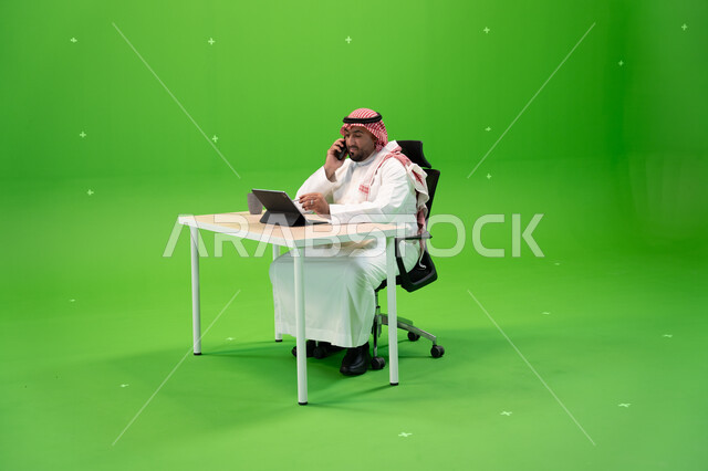 إدارة شؤون الأعمال وتنظيمها, إجراء مكالمة هاتفية عبر الهاتف المحمول, بورتريه لموظف عربي سعودي خليجي يرتدي الثوب السعودي التقليدي والشماغ يقوم بالعمل داخل مكتبه, استخدام جهاز التابليت لإنجاز مهام العمل, خلفية خضراء, كروما