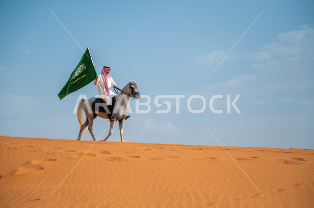 مشاعر الإنتماء وحب البلاد, هواية ركوب الخيل وشغف الفروسية، فارس عربي خليجي سعودي يركب فرس عربي أصيل يرفع علم السعودية في الصحراء، ذكرى اليوم الوطني لتوحيد المملكة ، العيد الوطني 23 سبتمبر، يوم العلم السعودي 11 مارس