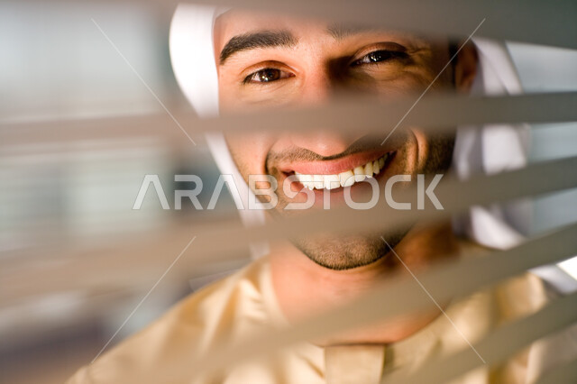 ايماءات السعادة والنظر إلى الكاميرا، صورة مقربة لرجل عربي خليجي اماراتي يرتدي الغترة والكندورة يقف خلف جدار زجاجي مخطط في مقر الشركة، تحقيق إستراتيجيات وأهداف العمل ،مهن ووظائف في الامارات العربيه المتحدة