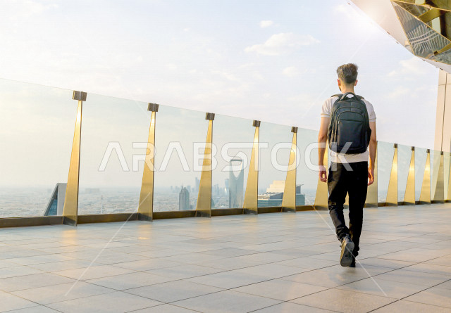 شاب سعودي سائح يحمل حقيبته على ظهره  ، يقف بشرفة عالية   ينظرالى ابراج الرياض ، اطلاله رائعة لأبراج الرياض ، ناطحات السحاب في المملكة العربية السعودية 